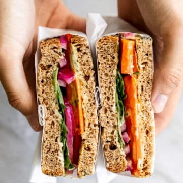 Hands holding roasted carrot sandwich.