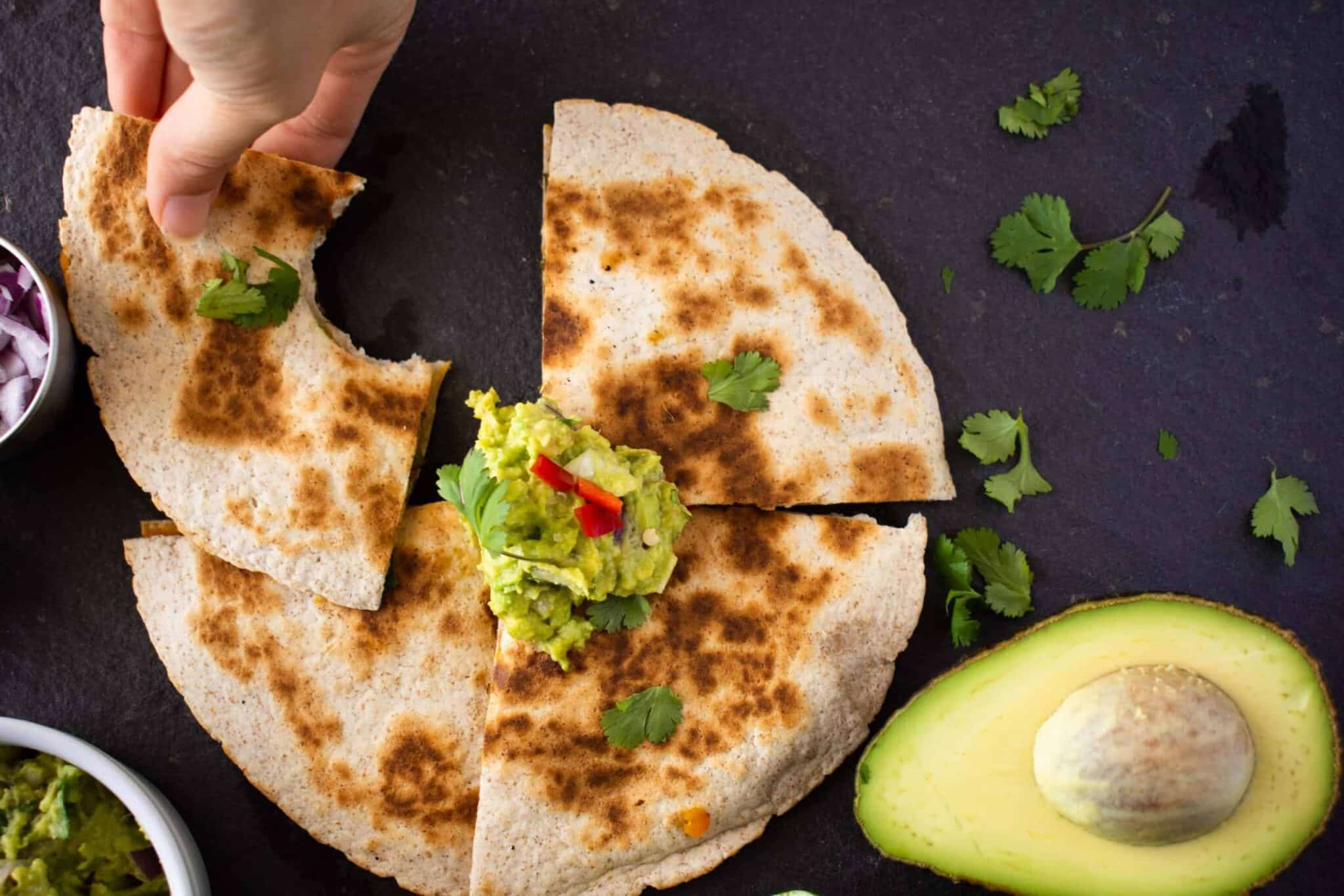 a vegan butternut squash quesadilla cut into quarters which a bite out of one piece.