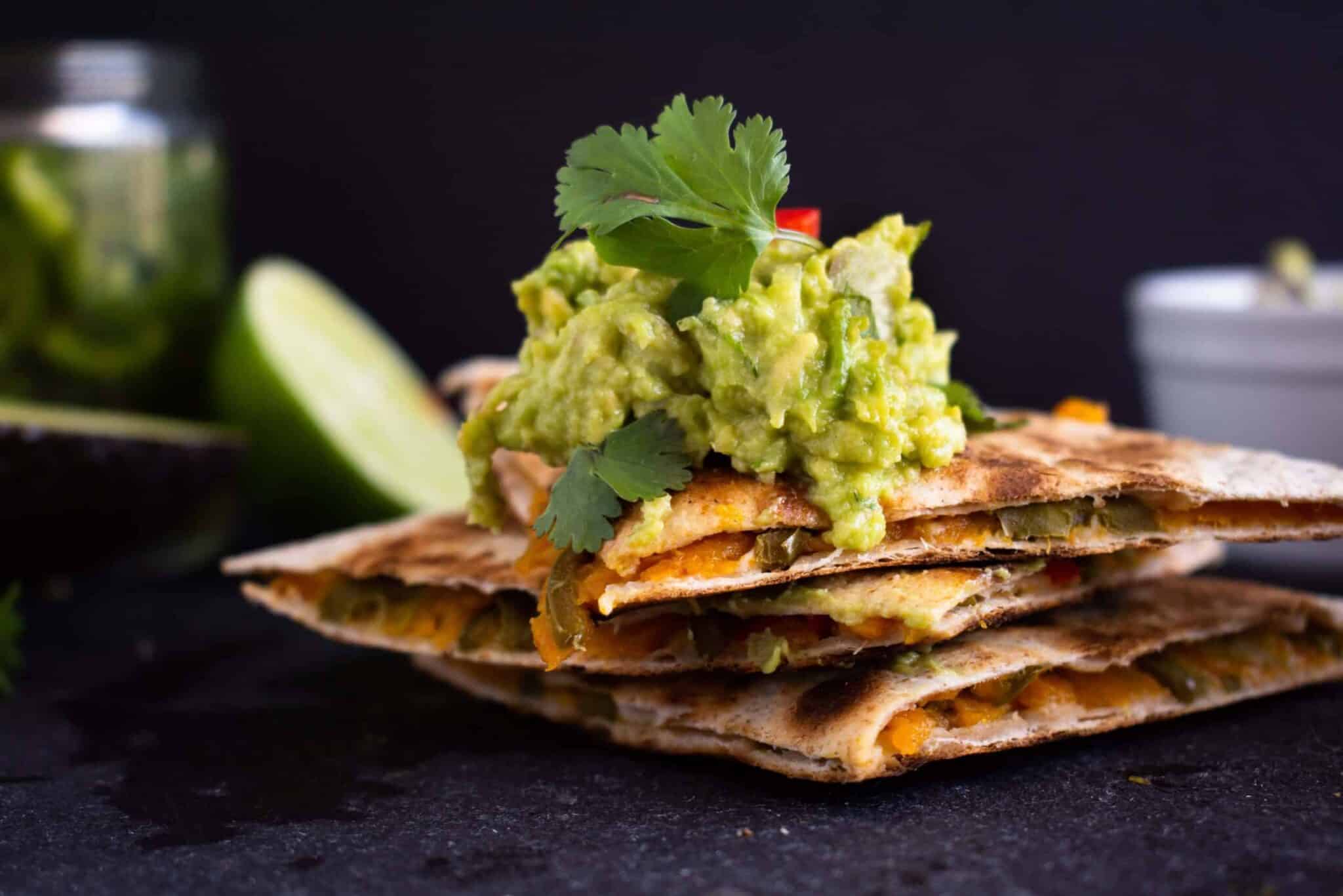 stacked butternut squash quesadillas covered in guacamole.