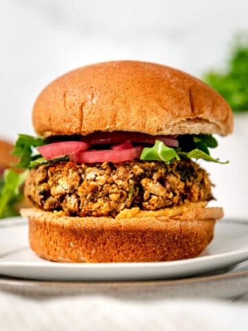 chickpea falafel burger on a whole wheat bun with hummus, arugula and pickled red onions