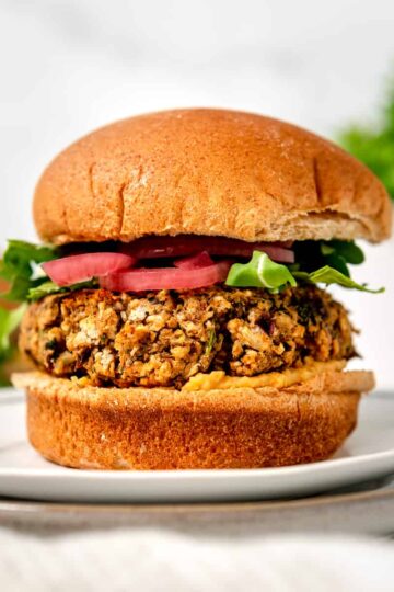 chickpea falafel burger on a whole wheat bun with hummus, arugula and pickled red onions.