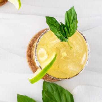 margarita in a glass garnished with a leaf of basil and a lime.