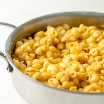 close up of macaroni noodles in a stainless pan covered in velvety yellow butternut squash cheese