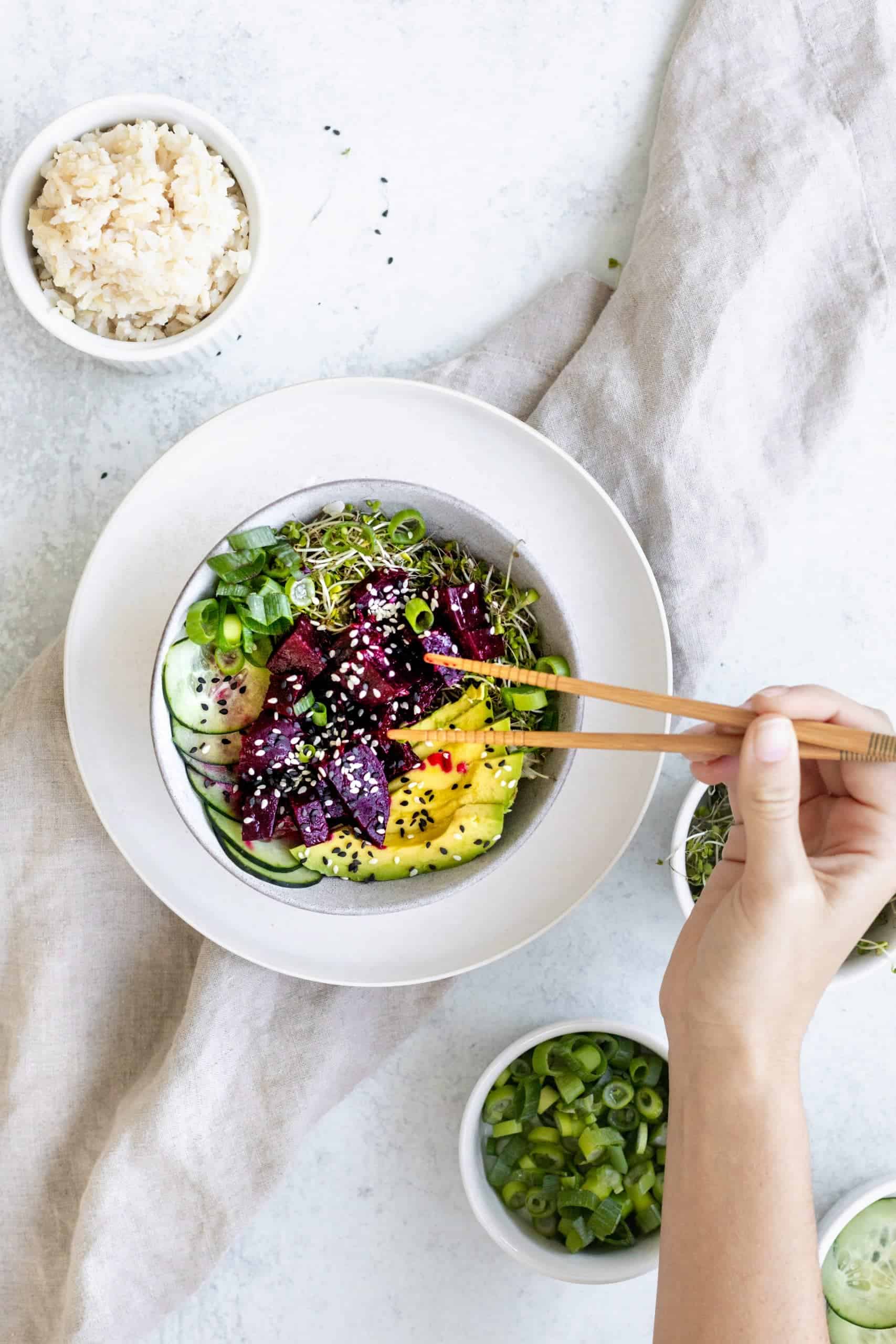 Vegan Beet Poke Bowl with avocado, scallions, rice. Chopsticks are reaching in to grab a cube of beet.