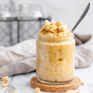 Macadamia Nut Butter in a jar with macadamia nuts sprinkled on top and on the table.