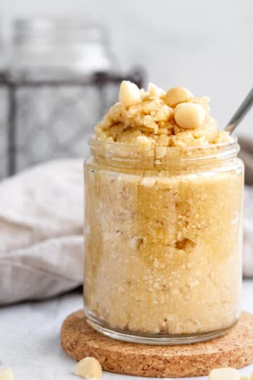 Macadamia Nut Butter in a jar with macadamia nuts sprinkled on top and on the table.