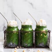 3 mason jars with green smoothie topped with whipped cream and coconut flakes