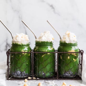 3 mason jars with green smoothie topped with whipped cream and coconut flakes.