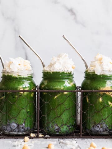 3 mason jars with green smoothie topped with whipped cream and coconut flakes