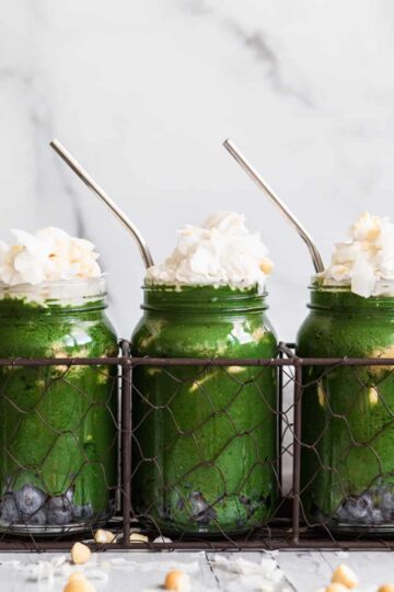 3 mason jars with green smoothie topped with whipped cream and coconut flakes.