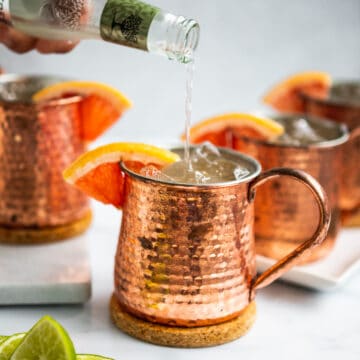 pouring ginger beer into a copper mug with grapefruit wedge and ice.