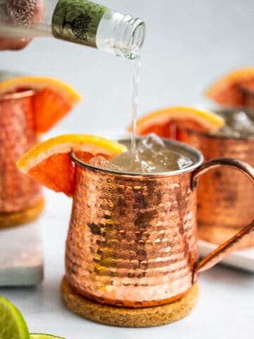 pouring ginger beer into a copper mug with grapefruit wedge and ice
