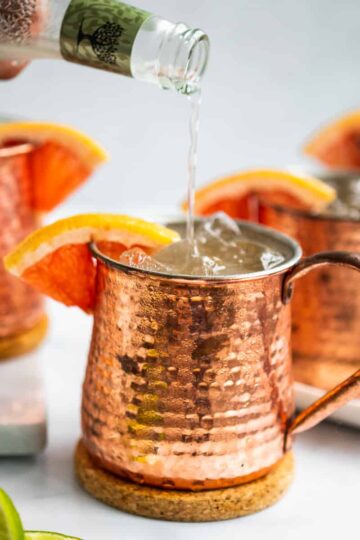 pouring ginger beer into a copper mug with grapefruit wedge and ice.