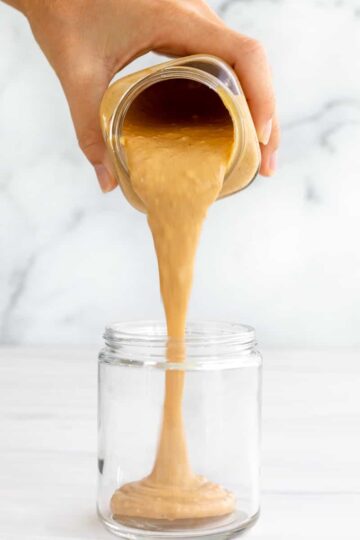 peanut butter sauce pouring into a jar in a long thick stream.