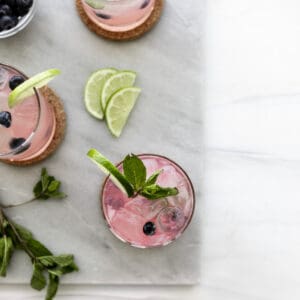 Blueberry Mint Mojito Recipe with lime wedges, mint leaves and blueberries. Ice cubes in the glass.