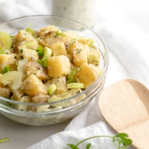 cilantro vegan potato salad in a glass bowl with a wooden spoon.