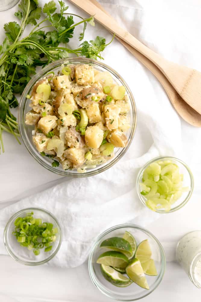 Plant Based Cilantro Lime Potato Salad overhead with scallions, limes and fresh cilantro. 