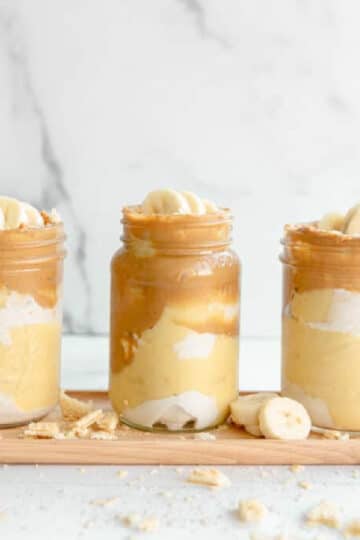 vegan peanut butter pudding in a glass mason jar. sliced banana and cream on the top of the pudding.