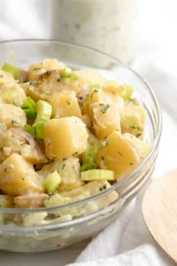 cilantro vegan potato salad in a glass bowl with a wooden spoon.