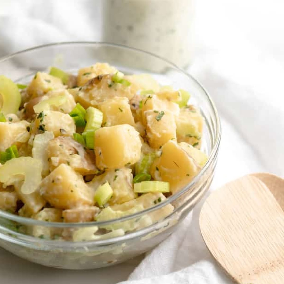 cilantro vegan potato salad in a glass bowl with a wooden spoon.