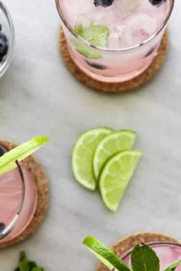 Blueberry Mint Mojito Recipe with lime wedges, mint leaves and blueberries. Ice cubes in the glass.