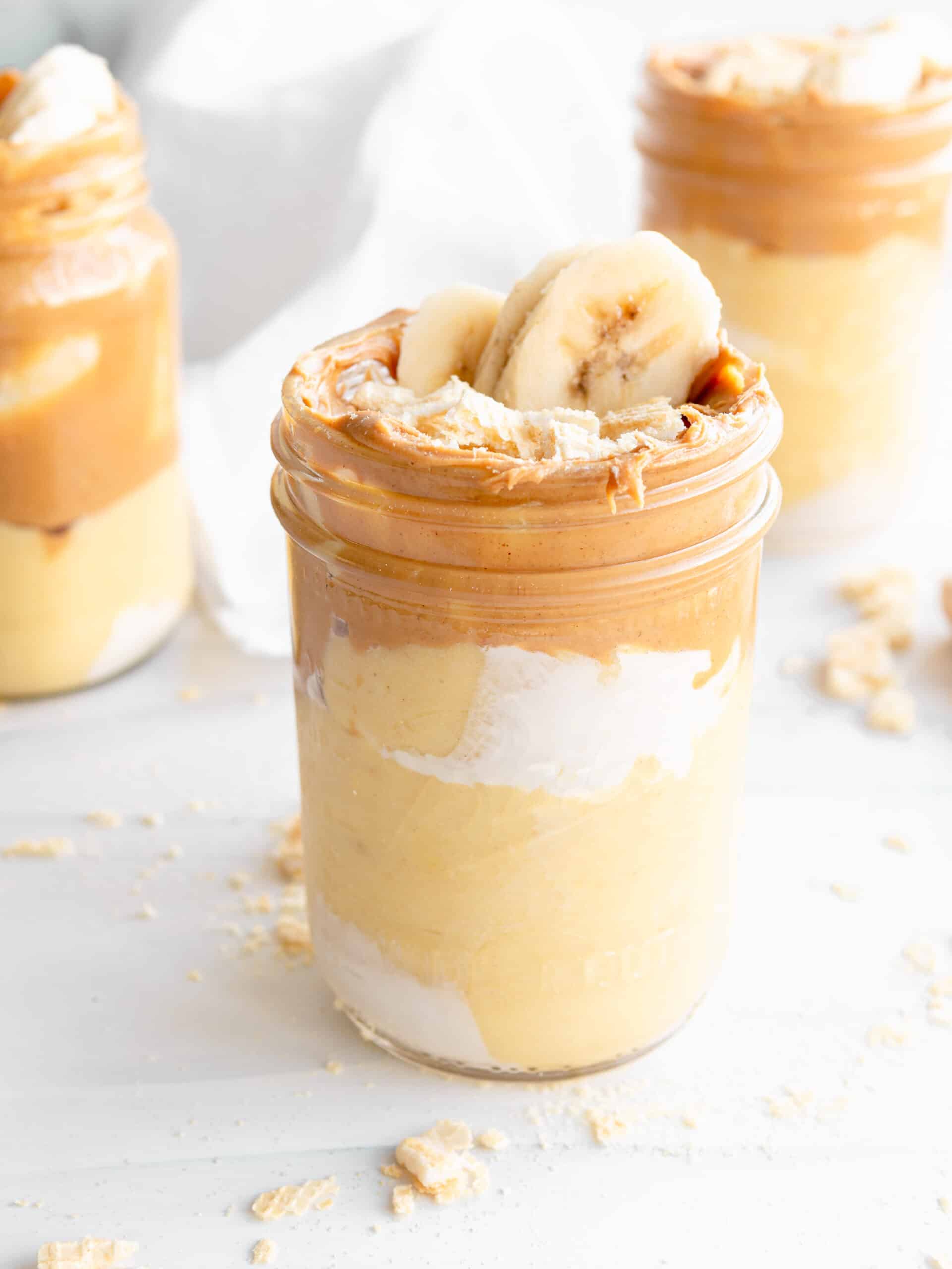 3 mason jars layered with cream, banana pudding and peanut butter.