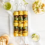 Grilled Veggie Kebabs - Corn, mushrooms, zucchini, and bell peppers on a metal skewer drizzled with chimichurri sauce, and accompanied by peanut butter banana pudding and potato salad.