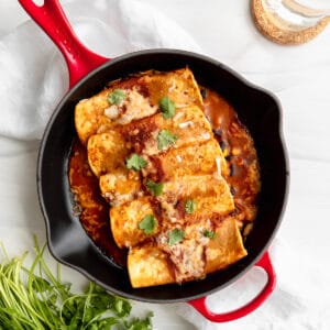 Black Bean Enchiladas overhead in a red cast iron skillet with cilantro garnish.