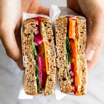 Hands holding roasted carrot sandwich