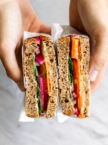 Hands holding roasted carrot sandwich