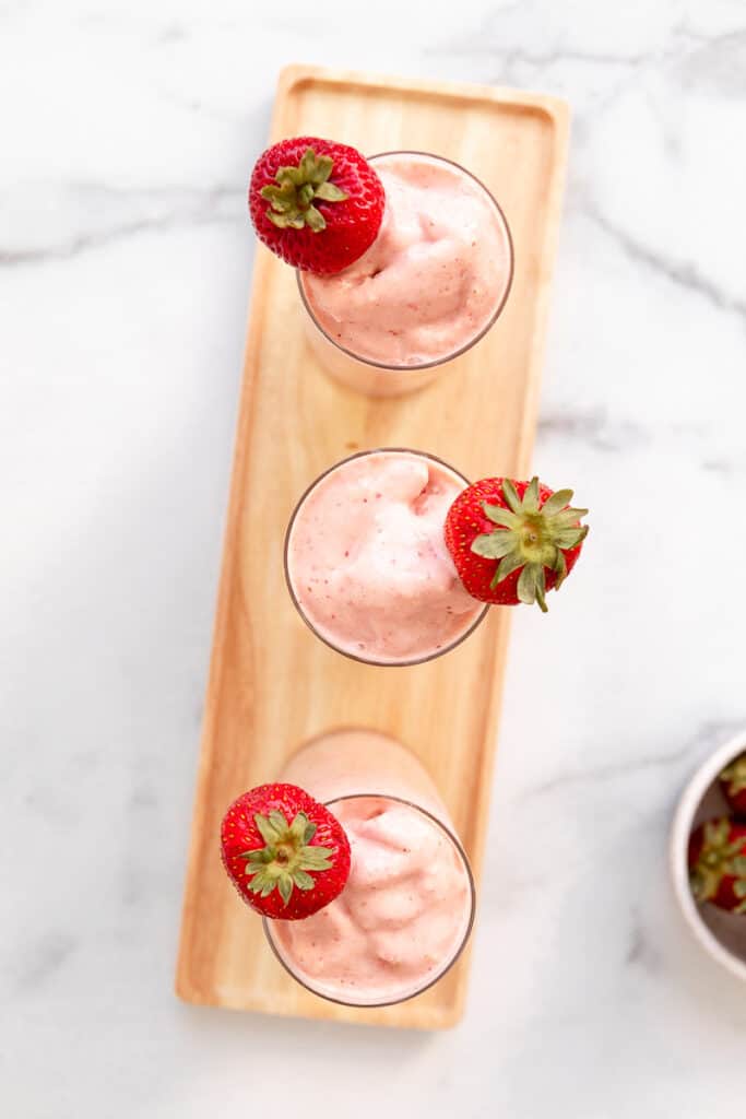 3 vegan strawberry mango smoothies with strawberry garnish on a tray
