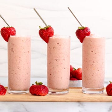 3 strawberry mango smoothie glasses with strawberry garnish and straw.