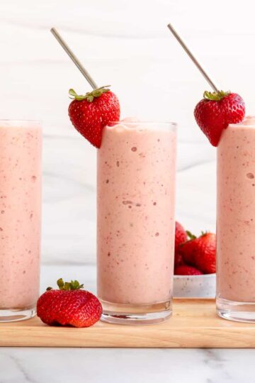 3 strawberry mango smoothie glasses with strawberry garnish and straw.