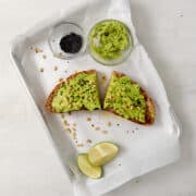 2 slices of avocado toast topped with pine nuts and black sesame seeds