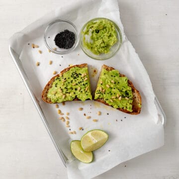 2 slices of avocado toast topped with pine nuts and black sesame seeds.