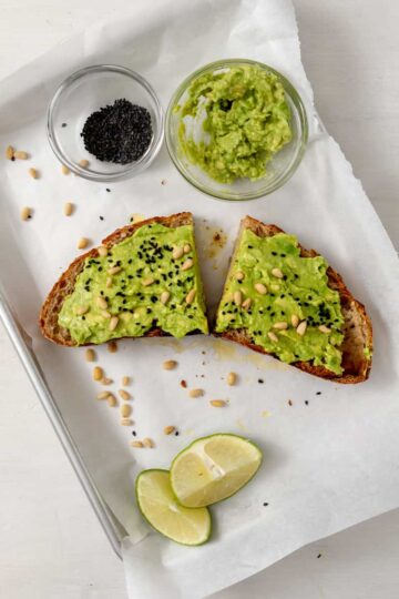 2 slices of avocado toast topped with pine nuts and black sesame seeds.