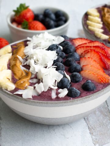 thick berry smoothie bowl topped with bananas, peanut butter, coconut flakes, blueberries and strawberries