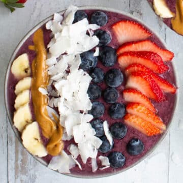 thick berry smoothie bowl topped with bananas, peanut butter, coconut flakes, blueberries and strawberries.