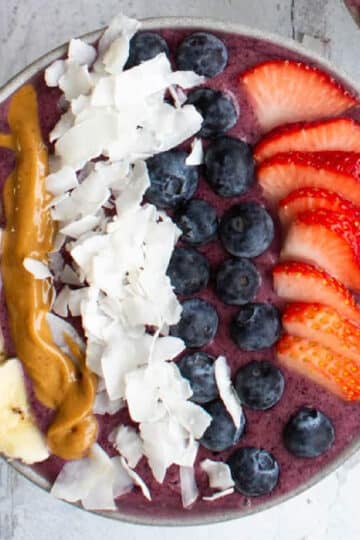 thick berry smoothie bowl topped with bananas, peanut butter, coconut flakes, blueberries and strawberries.