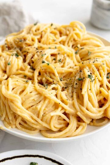 Butternut squash alfredo sauce on bucatini pasta with fresh thyme and black pepper.