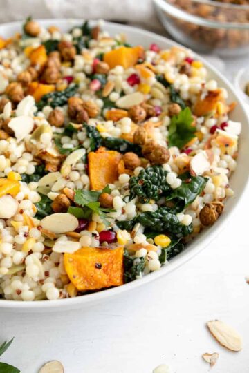 fall pearl couscous salad with butternut squash in a bowl with slivered almonds and pomegranate seeds.