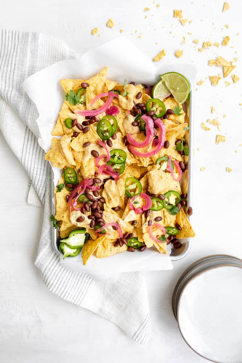 vegan nachos with yellow cheese sauce, pink pickled red onions, black beans, jalapeno slices and lime wedges. 