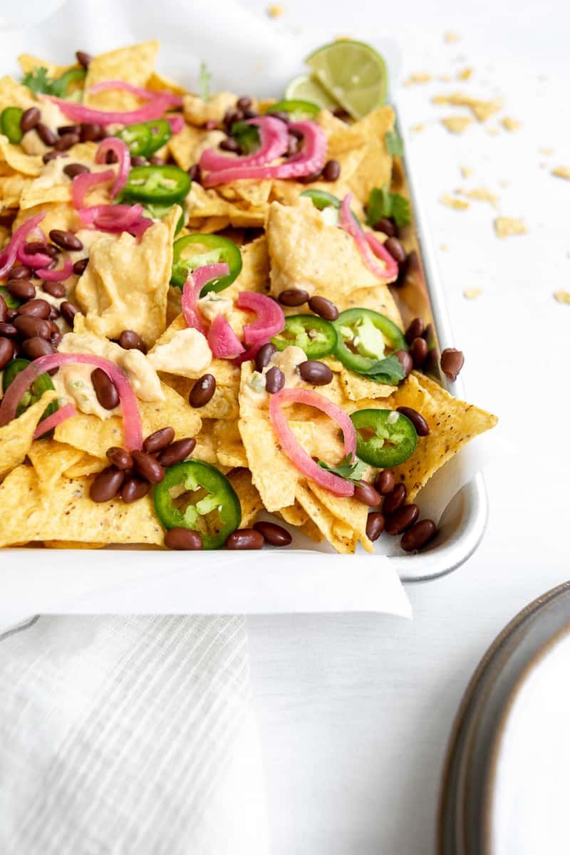 close up of vegan nachos with butternut squash cheese sauce, jalapenos, black beans, pickled red onions and lime wedge.