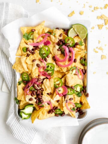 nachos with butternut squash cheese sauce, jalapenos, black beans, pickled red onions and lime wedge