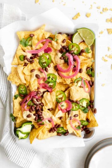 nachos with butternut squash cheese sauce, jalapenos, black beans, pickled red onions and lime wedge.