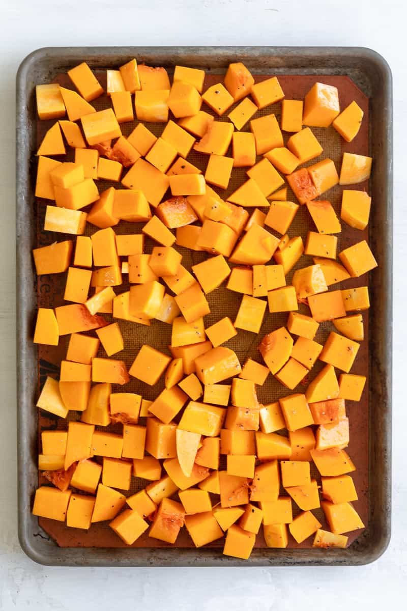 Butternut squash cubes a baking sheet, covered in oil, salt, and pepper
