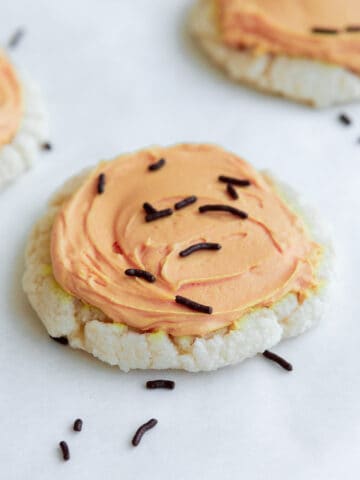 soft vegan sugar cookie with pale orange frosting and chocolate sprinkles
