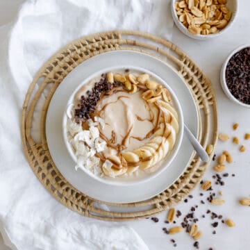 smoothie bowl with bananas, peanut butter drizzle, coconut flakes, and cacao nibs.