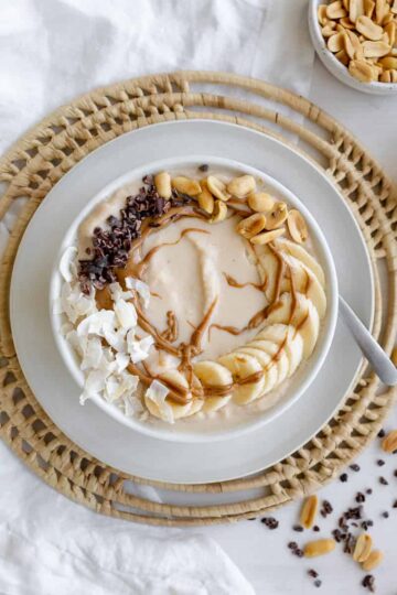 smoothie bowl with bananas, peanut butter drizzle, coconut flakes, and cacao nibs.