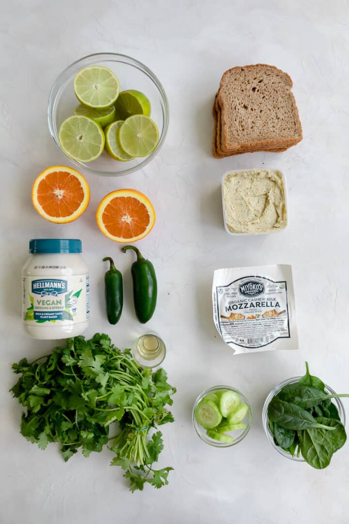 vegan green goddess sandwich ingredients: limes, oranges, vegan mayo, jalapeno, tequila, cilantro, bread, hummus, vegan mozzarella, cucumbers and spinach